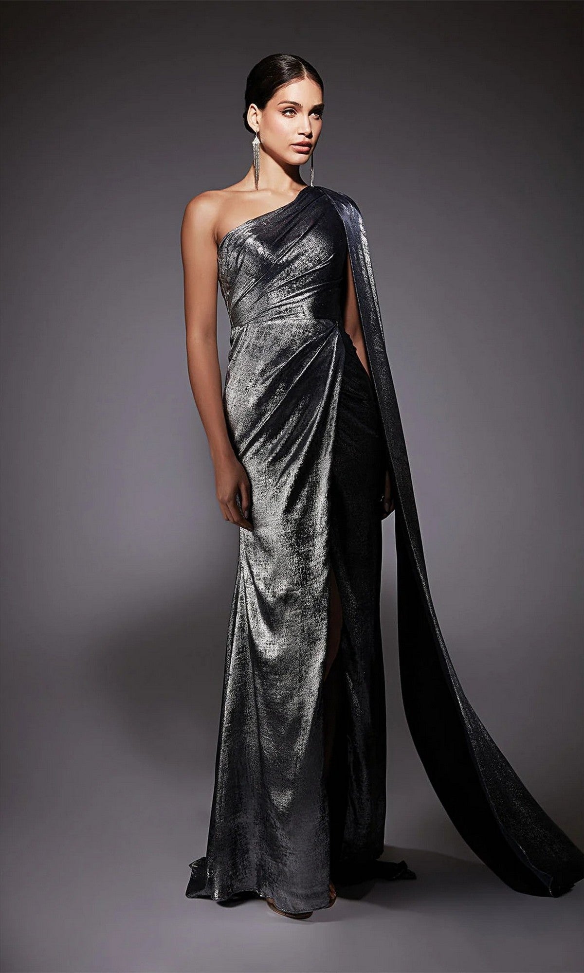A woman wearing the Alyce 27753 long formal dress, a metallic chiffon one-shoulder gown with a draped sleeve, stands against a neutral background.